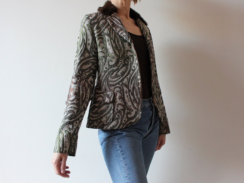 K&ouml;nnte beinhalten: Ein brauner und gr&uuml;ner gemusterter Blazer mit einem Kunstfellkragen. Der Blazer hat eine figurbetonte Silhouette und einen einreihigen Verschluss.