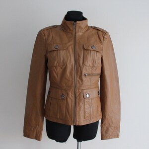 May include: A brown leather jacket with a zipper closure, two flap pockets on the chest, and two pockets on the waist.