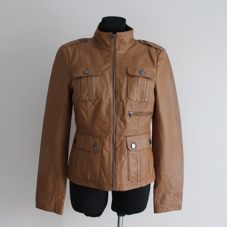 May include: A brown leather jacket with a zipper closure, two flap pockets on the chest, and two pockets on the waist.