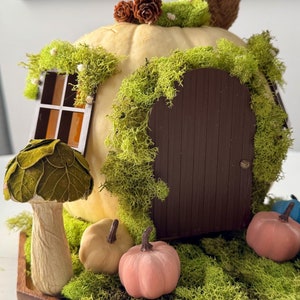 Peut inclure: Une maison de fée fantaisiste faite à partir d'une citrouille, avec une porte marron, une fenêtre et un toit en mousse verte. Une figurine d'écureuil est posée sur le dessus, avec des citrouilles miniatures et un champignon à la base. Le bouton de porte est en laiton.
