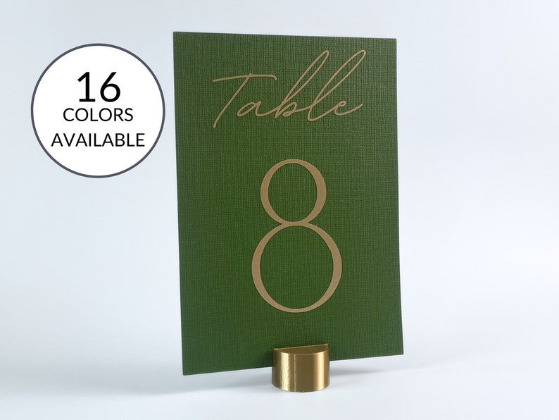 Brass table number holder in a circular holding a green 5x7 inch sign with the words "table eight".