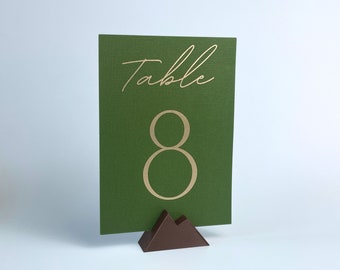 May include: Green table number card with gold lettering that says "Table 8" on a brown mountain-shaped stand.