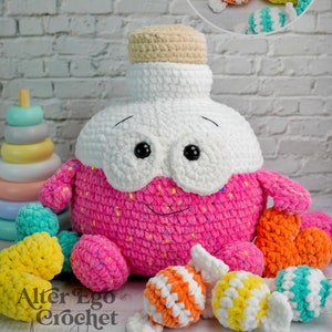 May include: A crocheted pink and white bottle shaped amigurumi toy with a smiling face. The toy is surrounded by smaller crocheted candy-shaped toys in various colors, including orange, yellow, and teal. The text "Alter Ego Crochet Amigurumi Designer" is visible in the bottom left corner of the image.