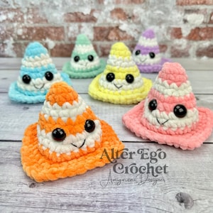 May include: Five crocheted cone-shaped plush toys with smiling faces. The cones are in various colors, including blue, green, yellow, purple, and orange. The toys are arranged in a row on a wooden surface. The text "Alter Ego Crochet Amigurumi Designer" is visible in the lower right corner of the image.