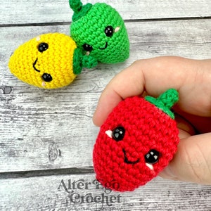 May include: Three crocheted amigurumi fruit toys: a yellow lemon, a green lime, and a red strawberry. Each fruit has a smiling face with black eyes and a white mouth.