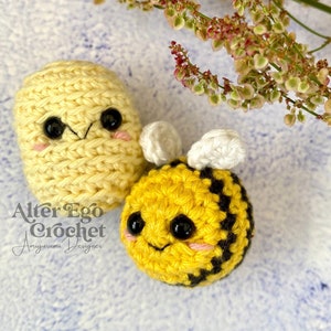May include: Two crocheted amigurumi toys: a yellow and black bee with white wings and a yellow egg-shaped character with a smiling face. The toys are on a blue and white background.