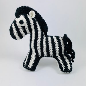 May include: A black and white striped crocheted zebra toy. The zebra has a long, curly tail and a black mane.