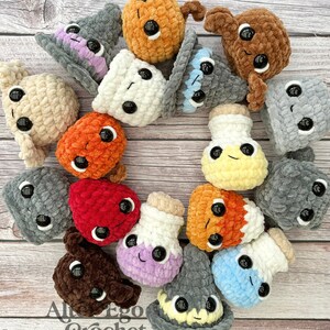 May include: A collection of 15 crocheted amigurumi toys in various colors and shapes, including a witch's hat, a potion bottle, and a mushroom. The toys have large eyes and are arranged in a circle on a wooden surface. The text "Al Ego Crochet Amigurumi Designer" is visible in the bottom left corner of the image.