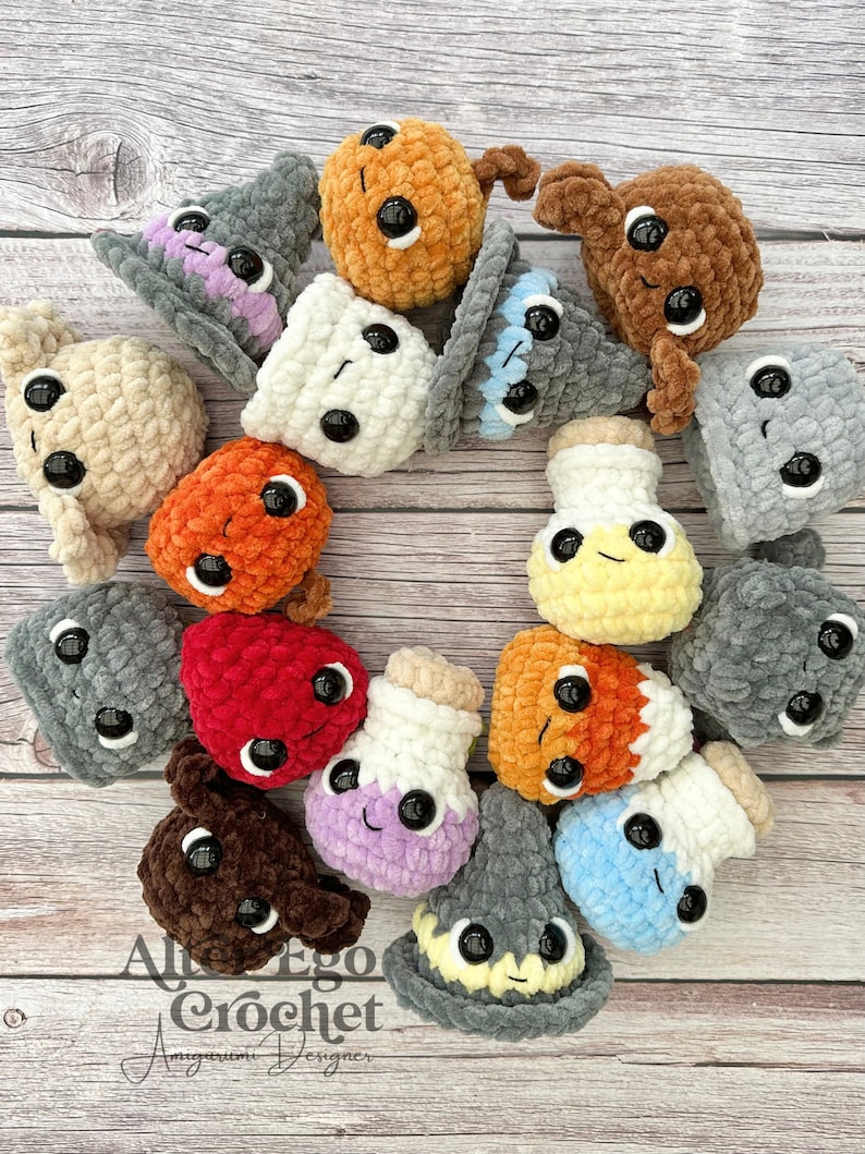 May include: A collection of 15 crocheted amigurumi toys in various colors and shapes, including a witch's hat, a potion bottle, and a mushroom. The toys have large eyes and are arranged in a circle on a wooden surface. The text "Al Ego Crochet Amigurumi Designer" is visible in the bottom left corner of the image.