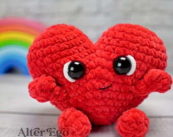 May include: A red crocheted heart-shaped amigurumi toy with a smiling face and large black eyes. The toy has small arms and legs.