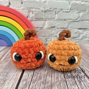 May include: Two crocheted pumpkins with smiling faces and googly eyes. The pumpkins are orange and brown and are sitting on a wooden surface.