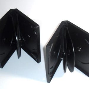 May include: Two open black DVD cases, each holding multiple discs. The cases are angled, revealing the disc holders and the shiny surfaces of the DVDs. The background is plain white.