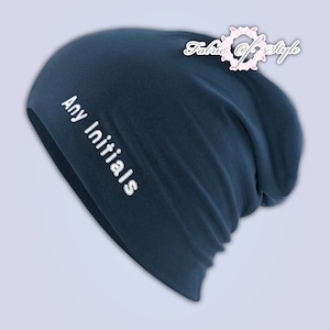 May include: A dark blue slouchy beanie hat featuring the white embroidered text Any Initials on the side. The hat has a soft, relaxed fit with a rounded crown and a folded hem. A logo with the text Fabric of Style is visible in the corner.