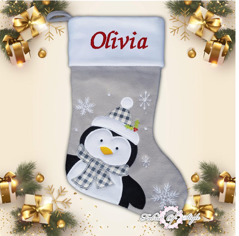 May include: A gray and white Christmas stocking with a penguin design. The stocking has the name "Olivia" embroidered on the cuff.