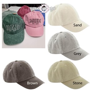 May include: A collection of six-panel baseball caps in various colors including green, pink, sand, grey, brown, and stone. The green cap features the embroidered text DAD EST. 2026 and the pink cap features the embroidered text MOM EST. 2026.