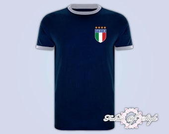 Pode incluir: Uma camiseta azul marinho com gola branca e um brasão de futebol italiano branco e azul com a palavra "ITALIA" e cinco estrelas douradas.
