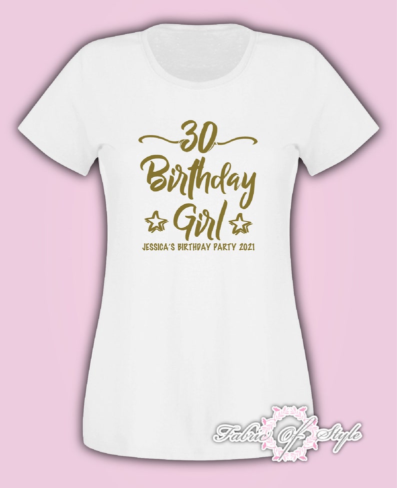 Może przedstawiać: Biała koszulka z złotym napisem "30 Birthday Girl" z dwiema złotymi gwiazdkami po obu stronach słowa "Girl". Pod gł&oacute;wnym napisem znajduje się tekst "Jessica's Birthday Party 2021".