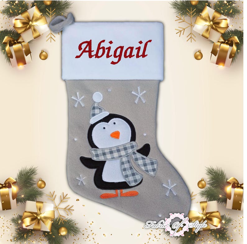 May include: A gray and white Christmas stocking with a penguin design and the name "Abigail" embroidered on the top.