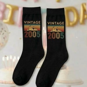 Peut inclure: Paire de chaussettes noires avec un design vintage. Le mot "VINTAGE" est imprimé au-dessus du chiffre "2005" dans un style rétro. Les chaussettes sont probablement un cadeau d'anniversaire.