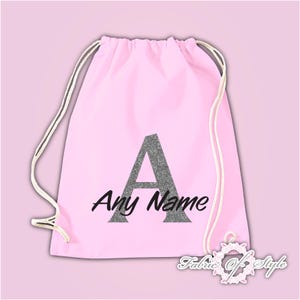 May include: Pink drawstring bag with a silver glitter letter A and the text "Any Name" in black.