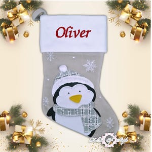 May include: A gray and white Christmas stocking with a penguin design. The stocking has a white cuff with the name "Oliver" embroidered in red.