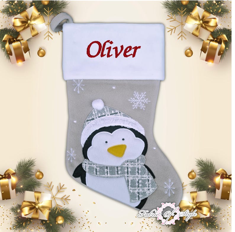May include: A gray and white Christmas stocking with a penguin design. The stocking has a white cuff with the name "Oliver" embroidered in red.