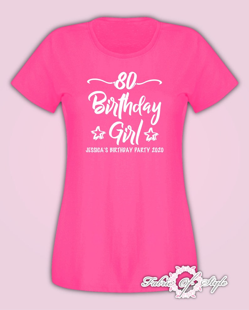 May include: Pink t-shirt with white text that says "80 Birthday Girl" with two stars on either side of the word "Girl". The text below says "Jessica's Birthday Party 2020".
