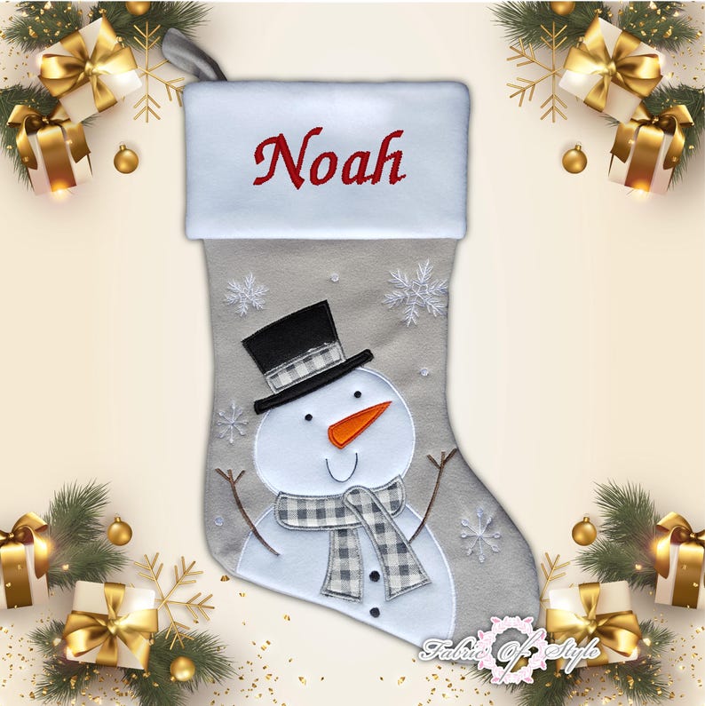 May include: A gray and white Christmas stocking with a snowman design. The stocking has a white cuff with the name "Noah" embroidered in red.