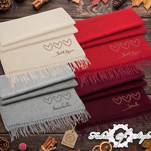 May include: Four folded scarves in cream, red, grey, and burgundy, each featuring three embroidered heart outlines and a personalised name. The cream and red scarves display the text Short Name, while the grey and burgundy scarves show Annabelle and Sarah.