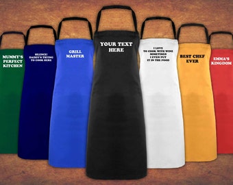 May include: A set of ten personalized aprons in various colors, including green, blue, black, white, yellow, and red. Each apron features a different humorous saying, such as "Mummy's Perfect Kitchen", "Silence: Daddy's Trying to Cook Here", "Grill Master", "Your Text Here", "I Love to Cook with Wine Sometimes I Even Put it in the Food", "Best Chef Ever", and "Emma's Kingdom".