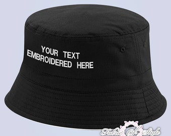 May include: A solid black bucket hat featuring white embroidered text on the front that reads YOUR TEXT EMBROIDERED HERE. The hat has a flat top, a downward-sloping brim with stitched detailing, and a clean, structured design for everyday wear.