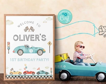 May include: A white sign with a blue car and the text "Welcome to Oliver's 1st Birthday Party!"  A child in a red and white striped shirt and blue overalls is sitting in a blue toy car. The background is a light brown wall with a blue airplane drawn on it.