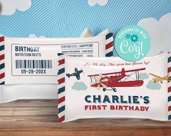 May include: Birthday-themed candy bar wrappers with a red, white, and blue design. The wrappers feature an airplane graphic and the text "Charlie's First Birthday." The background includes a blue sky with white clouds and chocolate heart-shaped lollipops.