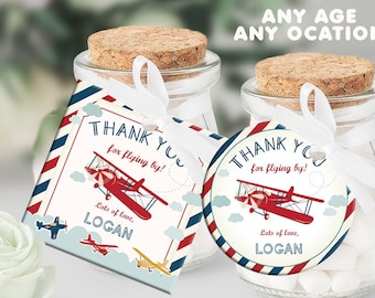 May include: Two small glass jars with cork lids and white ribbon tied around them. Each jar contains white candy. One jar has a square thank you tag with a red airplane and the text "THANK YOU for flying by! Lots of love, LOGAN". The other jar has a round thank you tag with a red airplane and the text "THANK YOU for flying by! Lots of love, LOGAN".