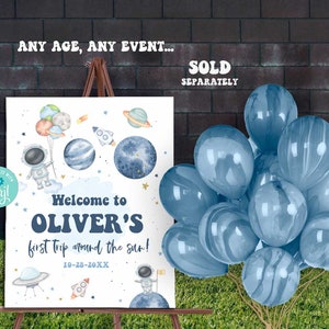 Pu&ograve; includere: Un cartello di benvenuto bianco con un astronauta blu, pianeti e stelle. Il testo recita "Benvenuto al primo viaggio di Oliver intorno al sole! 10-28-20XX".