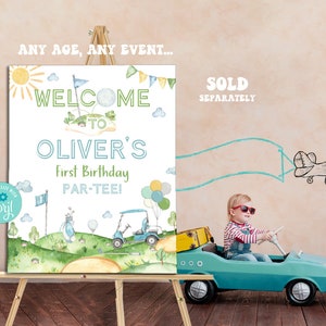 May include: A white welcome sign with a green golf course theme. The sign reads "Welcome to Oliver's First Birthday Par-Tee!" with a cartoon golf cart and golf clubs. The sign is on an easel and a child is driving a toy car in front of it.