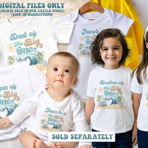 May include: Set of five white t-shirts with a beach theme and text that reads "Dad of the Big One", "Mom of the Big One", "Jacob's the Big One", "Brother of the Big One", and "Sister of the Big One".