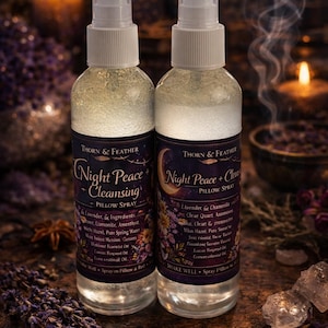 May include: Two clear glass spray bottles of Night Peace pillow spray with white tops and dark blue labels. The labels list ingredients and the brand name, Thorn & Feather. The background includes candles and dried flowers.