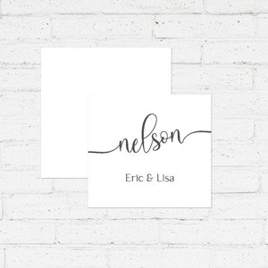 May include: A white card with the name "nelson" written in cursive script. Below the name, it says "Eric & Lisa". The card is on a white brick background.