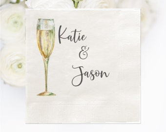 May include: White paper napkin with a champagne glass illustration and the text "Katie & Jason" in black cursive font.