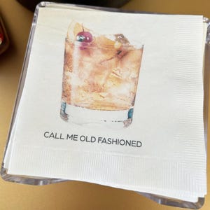 May include: A white napkin with a watercolor illustration of an old fashioned cocktail. The text "CALL ME OLD FASHIONED" is printed below the illustration.