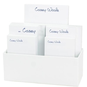 May include: White desk organizer with four stacks of personalized notepads. The notepads have the name "Casey Woods" written in blue ink.