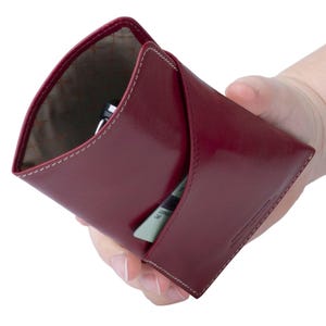 May include: A burgundy leather wallet with a flap closure and a white stitch detail. The wallet is open and shows a card slot and a pen holder.