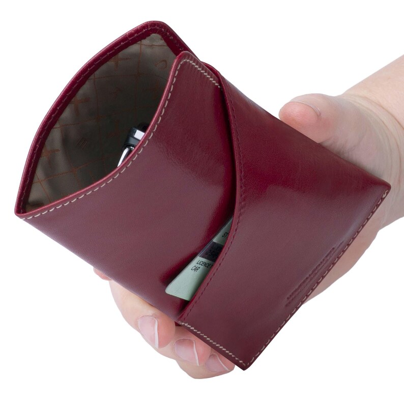 May include: A burgundy leather wallet with a flap closure and a white stitch detail. The wallet is open and shows a card slot and a pen holder.