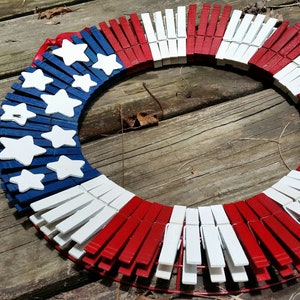May include: A red, white, and blue patriotic wreath made from wooden clothespins. The wreath is decorated with white stars on a blue background.