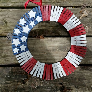 May include: A red, white, and blue American flag wreath made from clothespins. The wreath is decorated with white stars on a blue background.