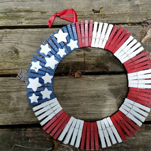 May include: A red, white, and blue American flag wreath made from clothespins. The wreath is decorated with white stars on a blue background.