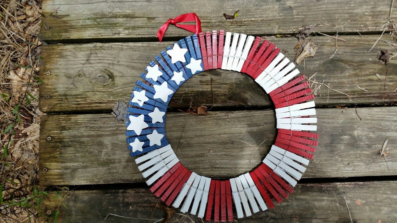 May include: A red, white, and blue American flag wreath made from clothespins. The wreath is decorated with white stars on a blue background.
