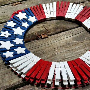 May include: A red, white, and blue patriotic wreath made from wooden clothespins. The wreath is decorated with white stars on a blue background.