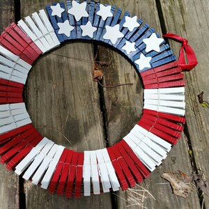 May include: A red, white, and blue wreath made from clothespins. The clothespins are painted to resemble the American flag. The wreath is decorated with white stars.